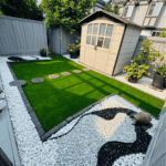 页面模板0_初版 25 Modern backyard landscaping with artificial turf, white gravel, black stone patterns, and a garden shed.