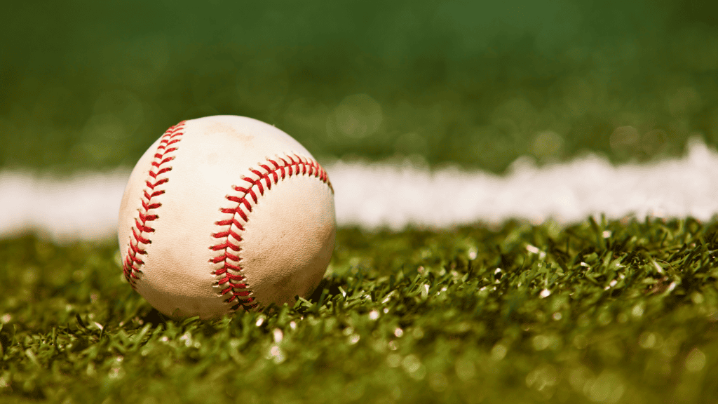 Close up of a baseball resting on the turf of a baseball field with green grass and a white field line in the background 1