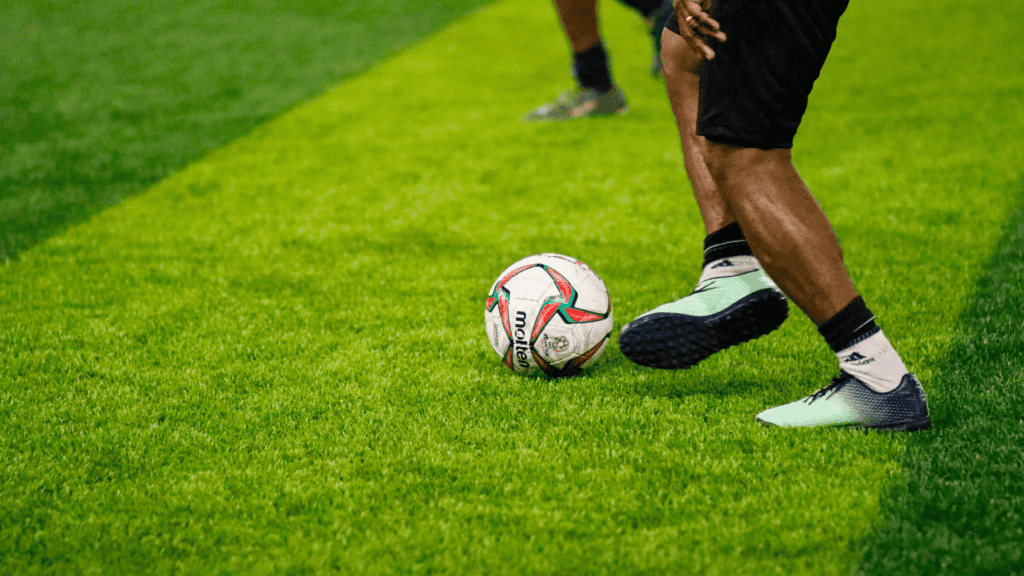 Close up of a soccer player kicking a ball on a green turf field