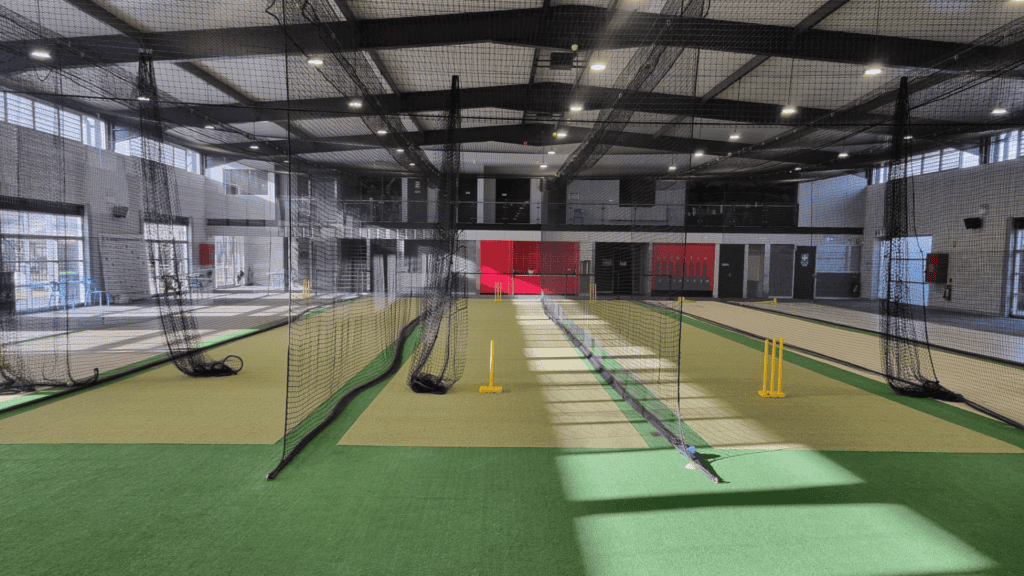 Indoor cricket turf with multiple nets stumps and bright lighting