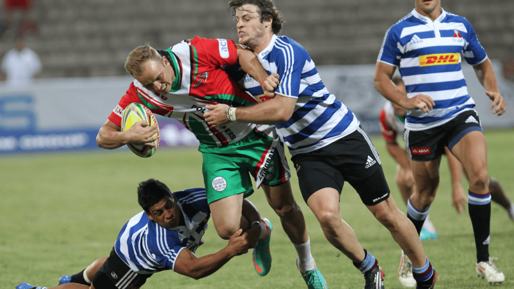 Rugby players in action on the field one player being tackled by two opponents