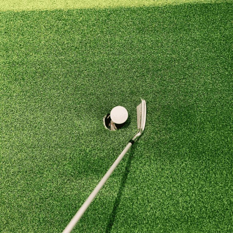 Indoor 1 close up of golf ball near hole on synthetic grass green with club ready for putting in residential setting
