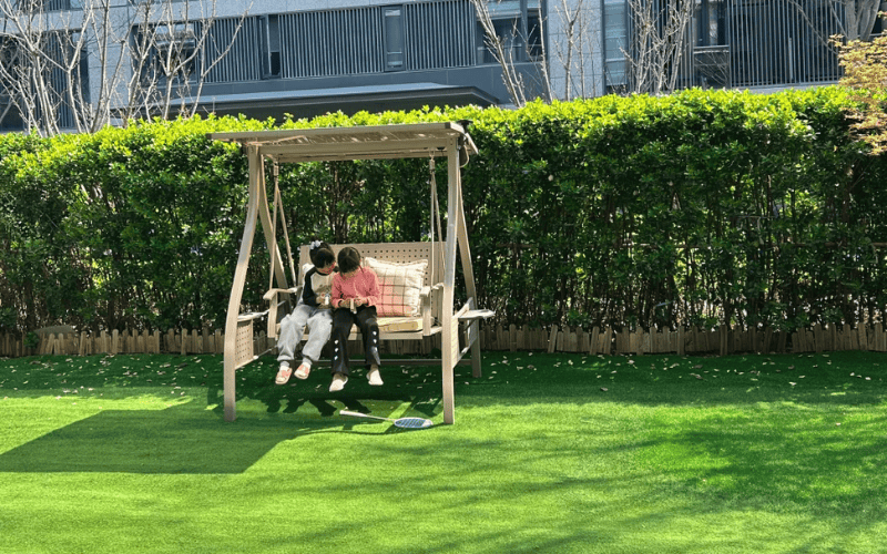 Children sitting on swing in residential yard with artificial grass lawn