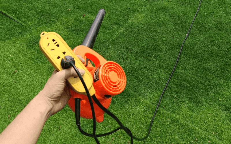 Person holding electric blower and extension cord on artificial grass surface