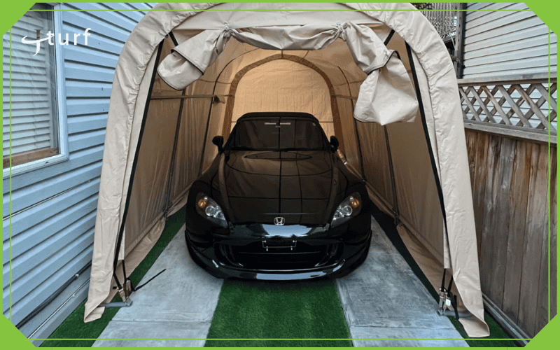 Garaje portátil con coche aparcado en entrada de césped artificial y camino de hormigón.