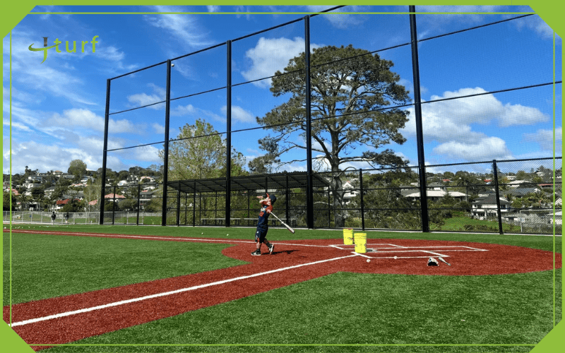 A Clear Look at the Cost to Build a Turf Baseball Field 4 Synthetic turf baseball field with high fence and batter practicing near home plate