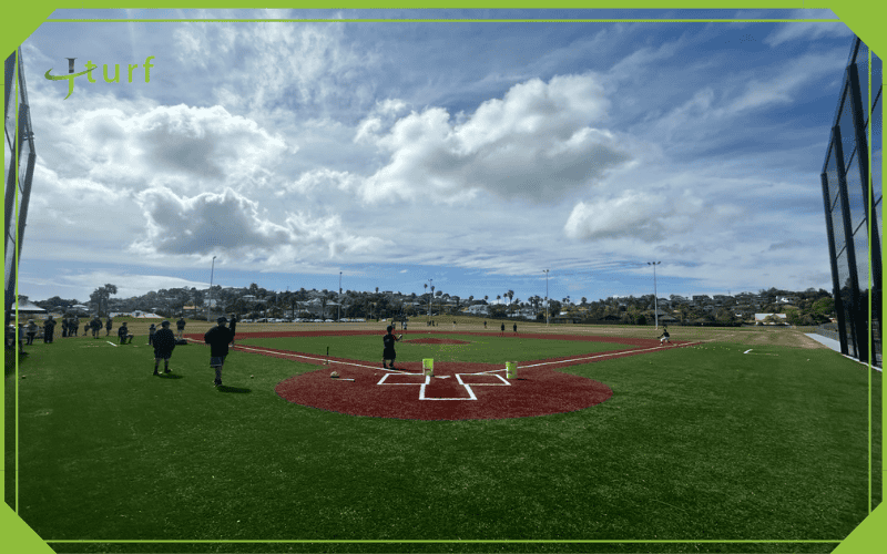 A Clear Look at the Cost to Build a Turf Baseball Field 1 Wide angle shot of a turf baseball field with players practicing under a cloudy sky