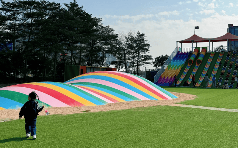 Acolchado de césped para áreas de juego 101 para superficies más seguras y suaves 2 Parque infantil inflable colorido con tobogán arcoíris sobre césped sintético