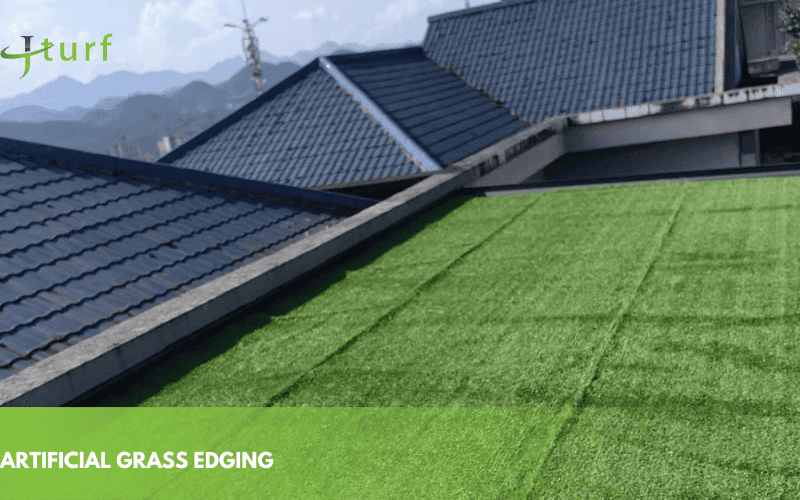A rooftop with artificial grass, featuring green turf beside dark-colored tiled roofs and distant mountains under a blue sky.