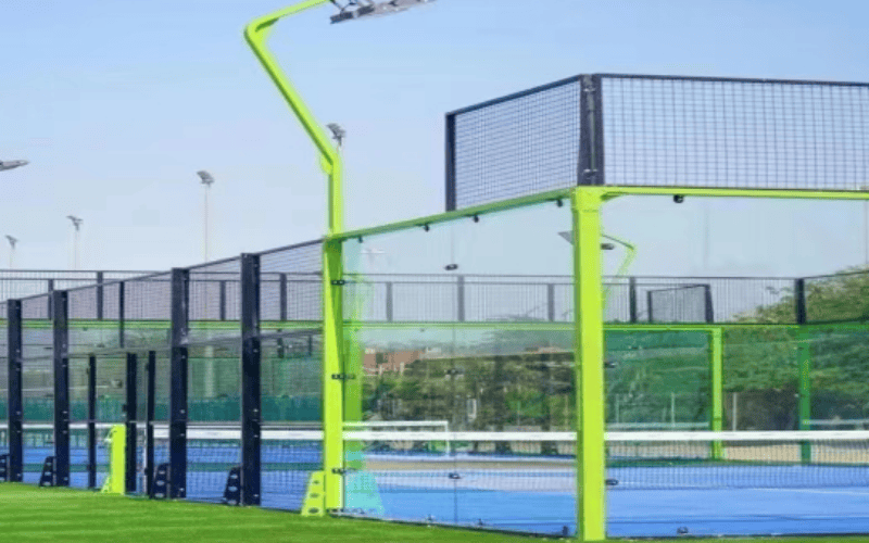 Pista de pádel exterior con césped azul y marco de acero verde.