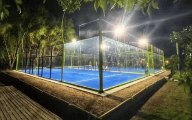 Pista de pádel exterior con césped azul iluminada por la noche.