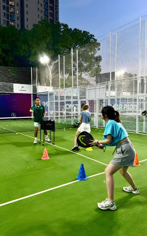 Players practicing on a vibrant Padel Court System, surrounded by colorful cones and under the guidance of an instructor. The court is enclosed with high netting, ensuring a safe and focused training environment.