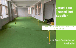 An indoor putting green with several flags and golf balls, surrounded by large windows and turf on the floor.