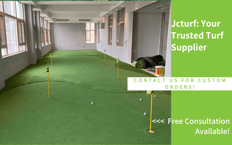 An indoor putting green with several flags and golf balls, surrounded by large windows and turf on the floor.