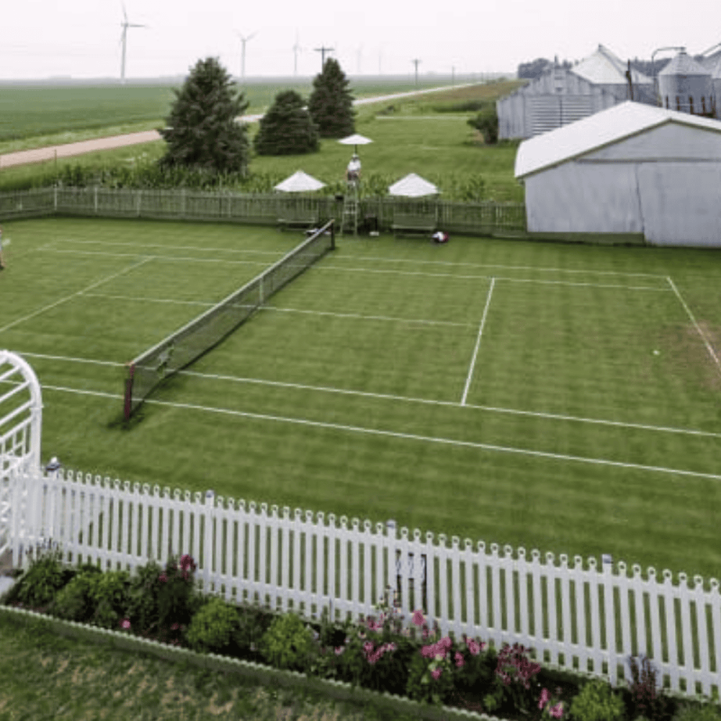 Two people playing tennis on garden tennis turf, surrounded by a white fence and lush greenery, highlighting a perfect blend of outdoor living and the sport Two people playing tennis on garden tennis turf, surrounded by a white fence and lush greenery, highlighting a perfect blend of outdoor living and the sport