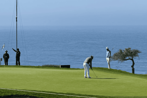 golfer putting on synthetic grass green with ocean view in the background at a coastal golf course golfer putting on synthetic grass green with ocean view in the background at a coastal golf course